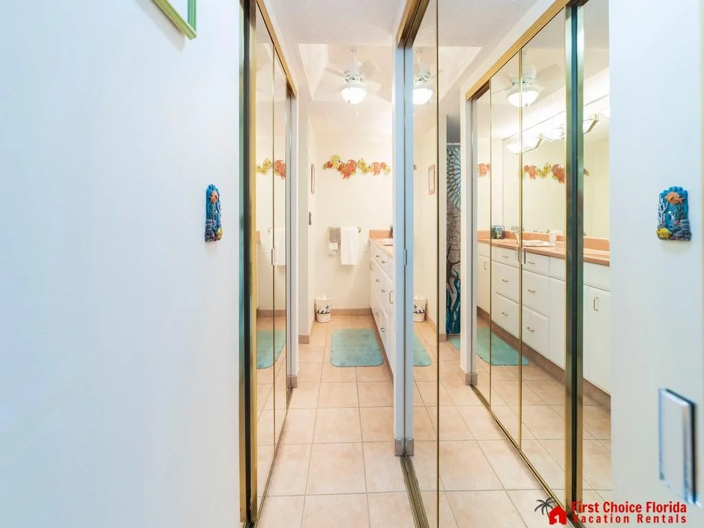 Hallway lined with mirrored sliding closet doors leads to a tiled bathroom with coral-colored countertops and blue bath mats.