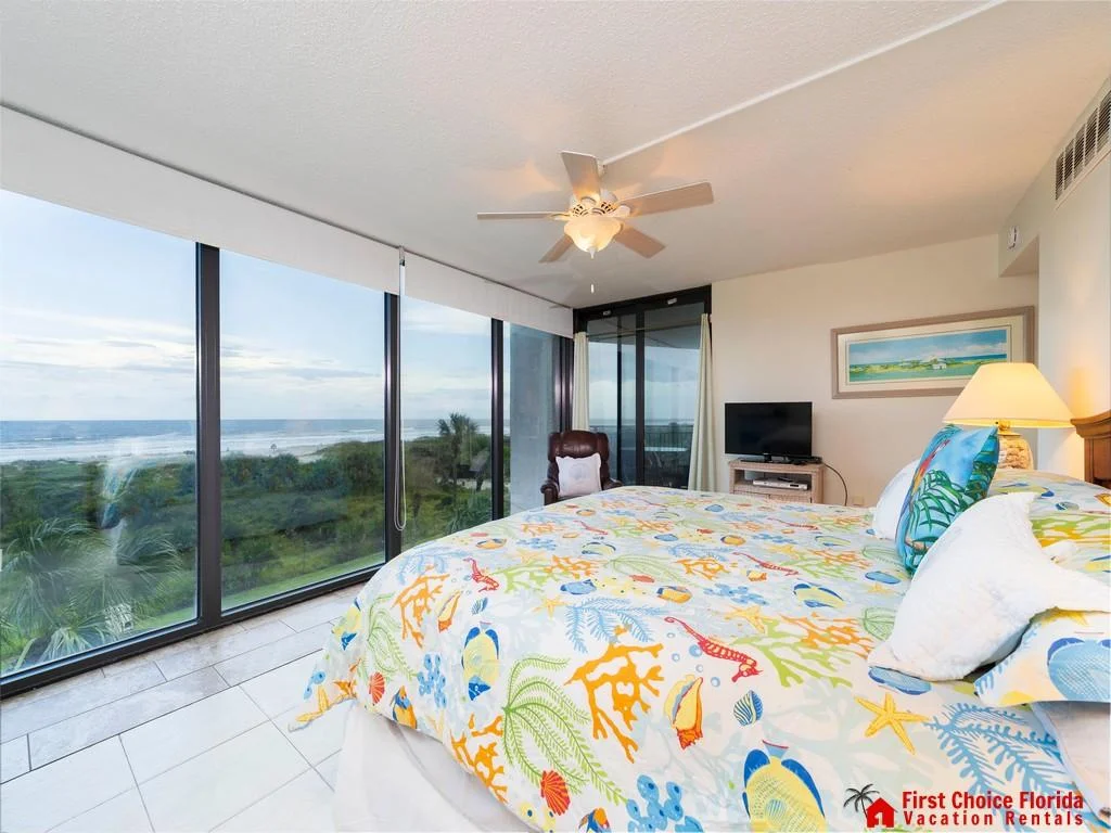 Oceanfront bedroom with tile floors, ceiling fan, leather recliner, and colorful sea life bedding.