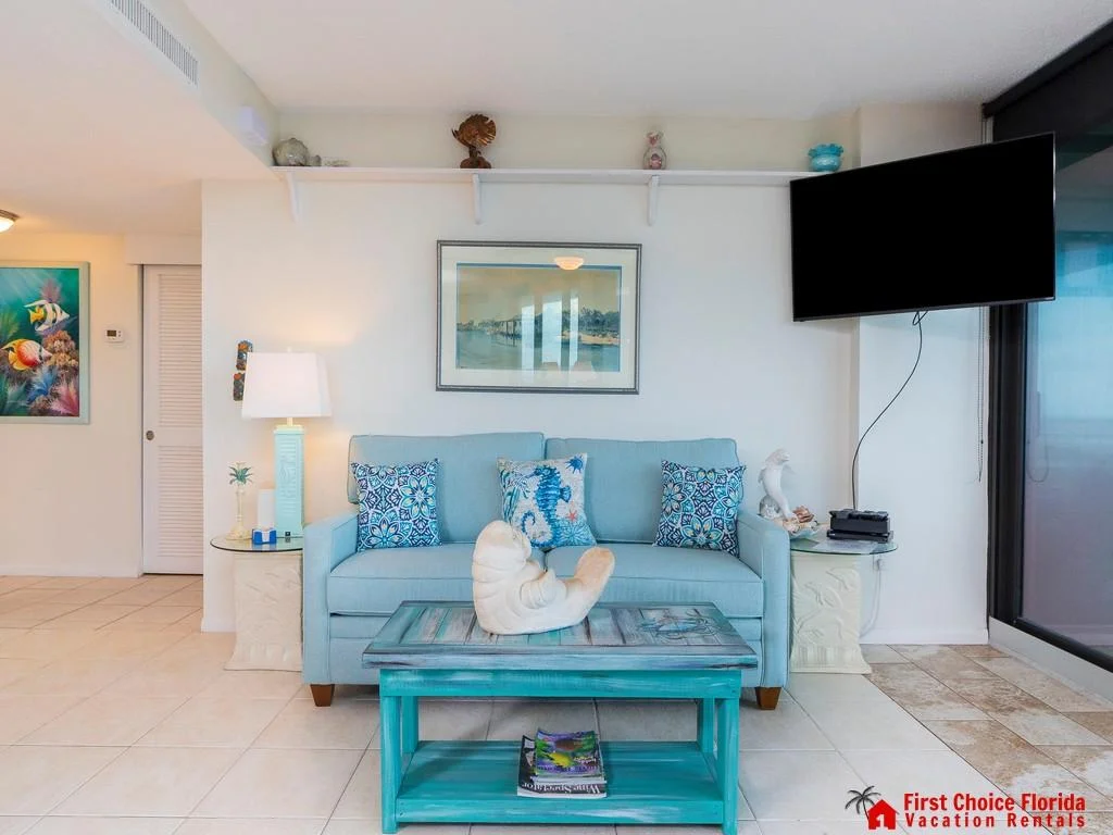 Light blue sofa with patterned pillows faces a wall-mounted TV beside sliding glass doors.