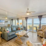 Living room with gray sofa, floral armchairs, wood coffee table, mirrored wall, and oceanfront balcony view.