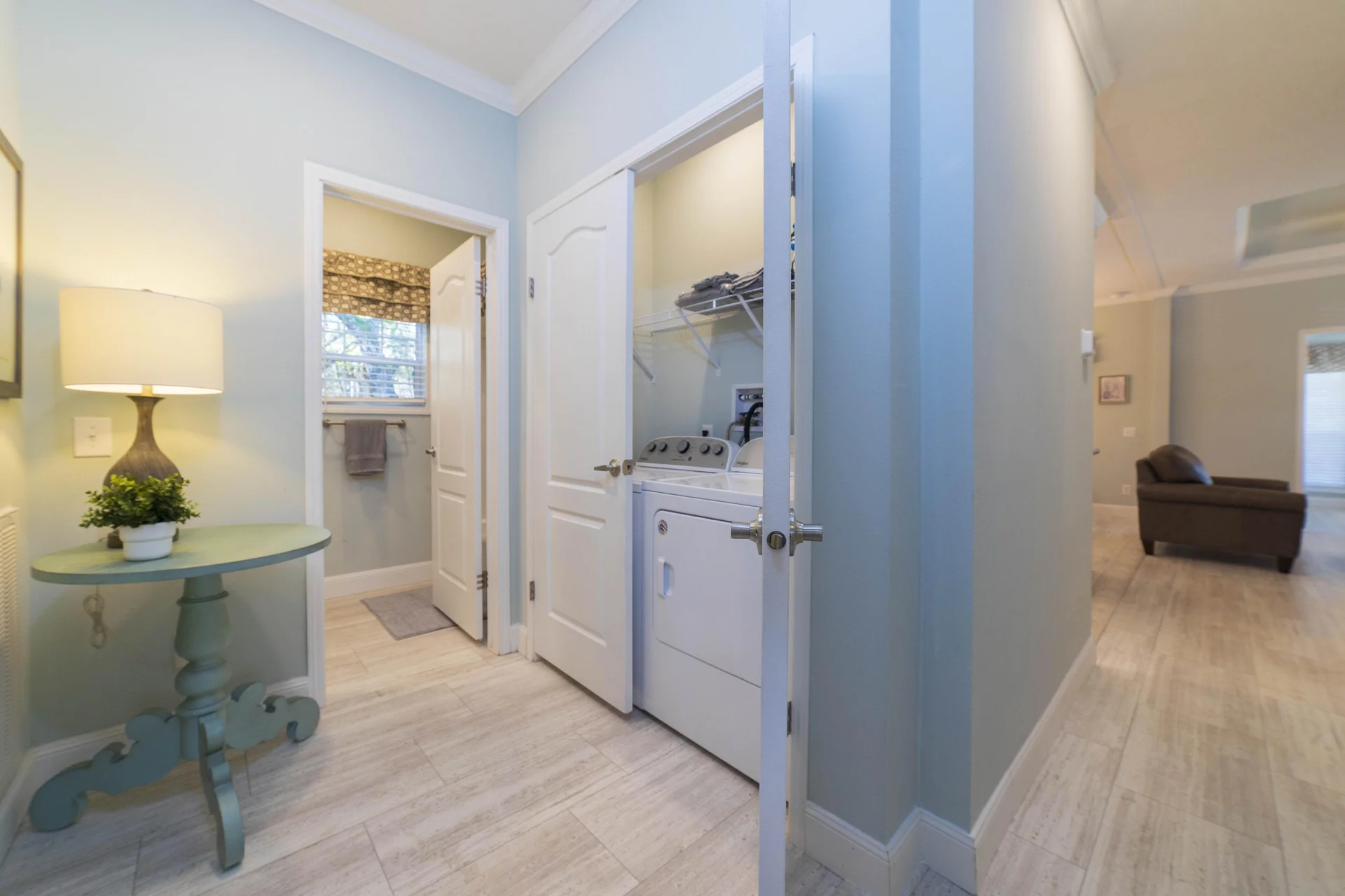 Laundry closet with stacked washer and dryer behind white double doors in hallway with pale wood-look tile flooring.