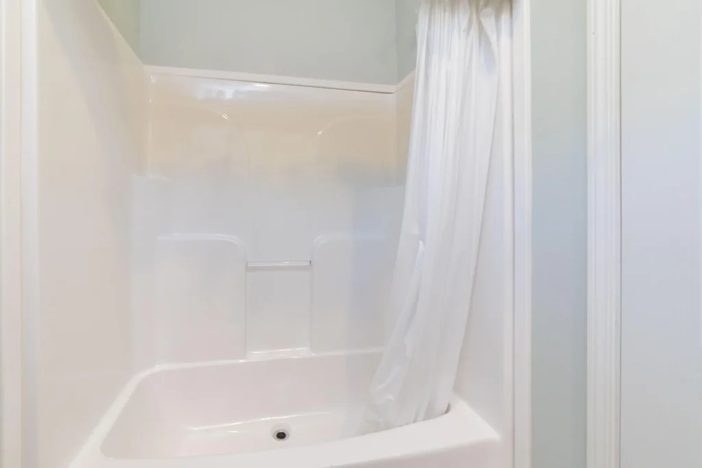 White acrylic bathtub and shower surround with built-in shelves and a white shower curtain.