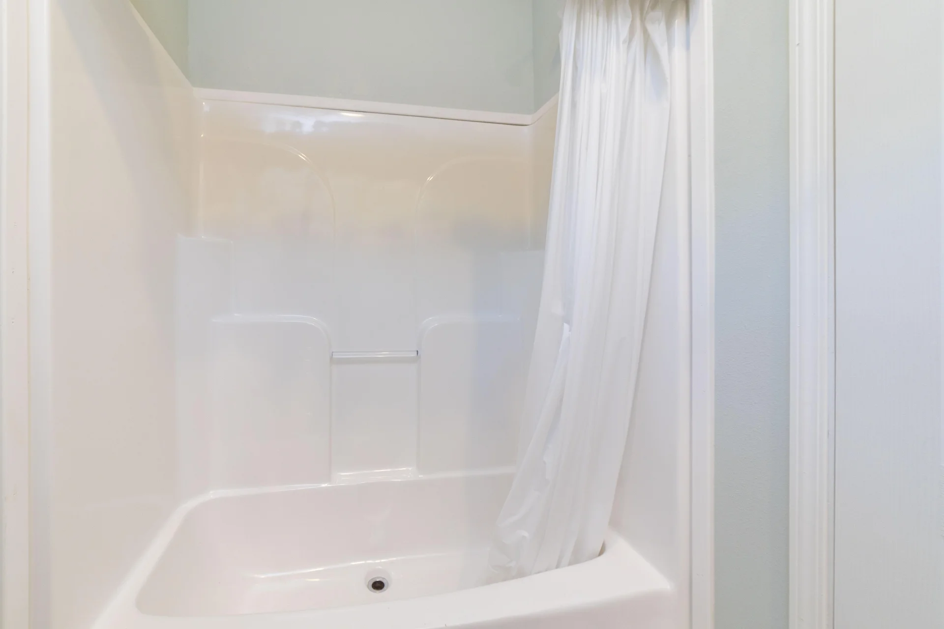 White acrylic bathtub and shower surround with built-in shelves and a white shower curtain.