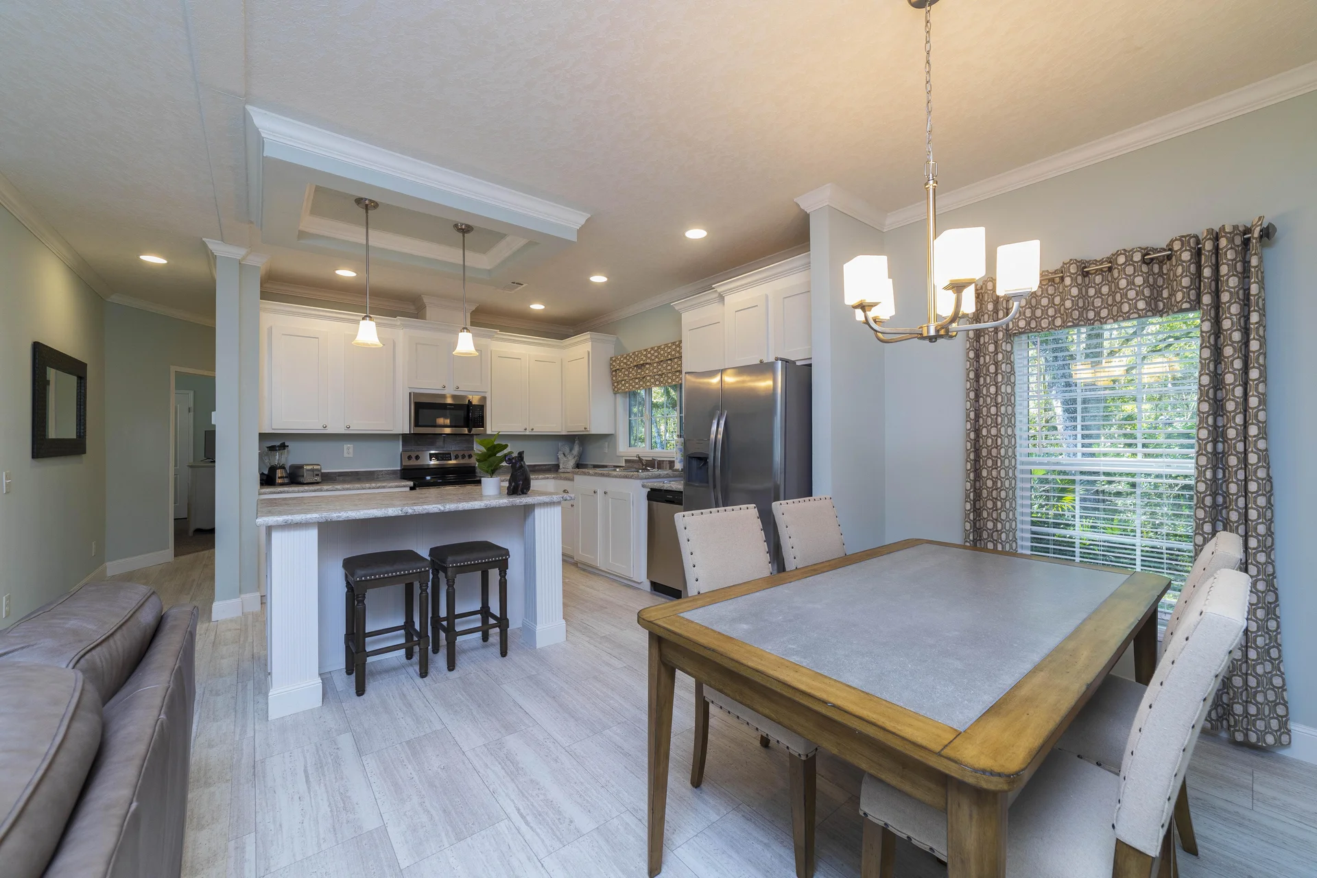 Dining area with wood-framed table, four upholstered chairs, and patterned curtains framing a window.