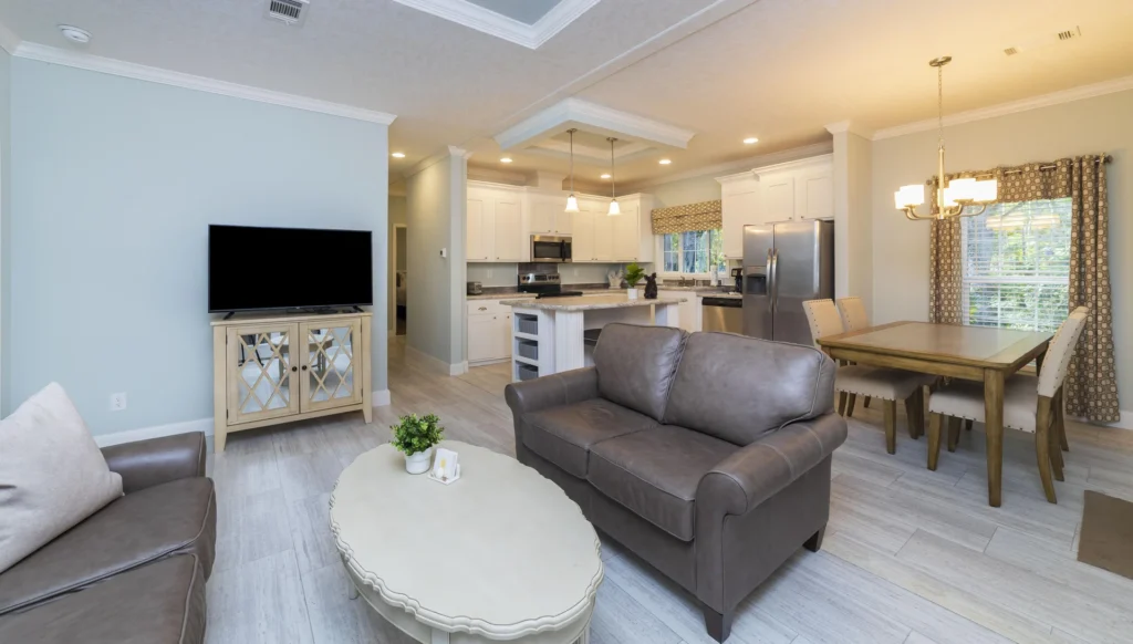 Open living area with gray leather sofas, an oval white coffee table, and a wall-mounted TV on a mirrored cabinet.