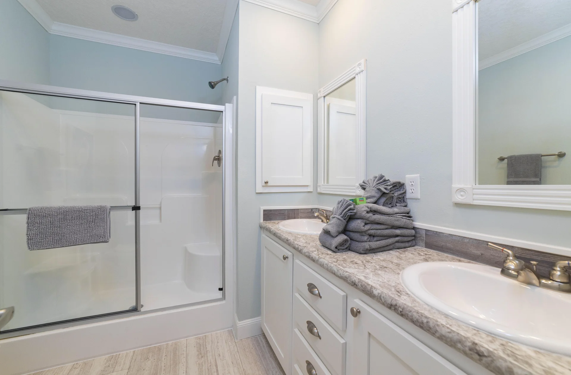 Bathroom with dual sinks set in granite countertop, white cabinetry, and a glass-enclosed shower with chrome fixtures.