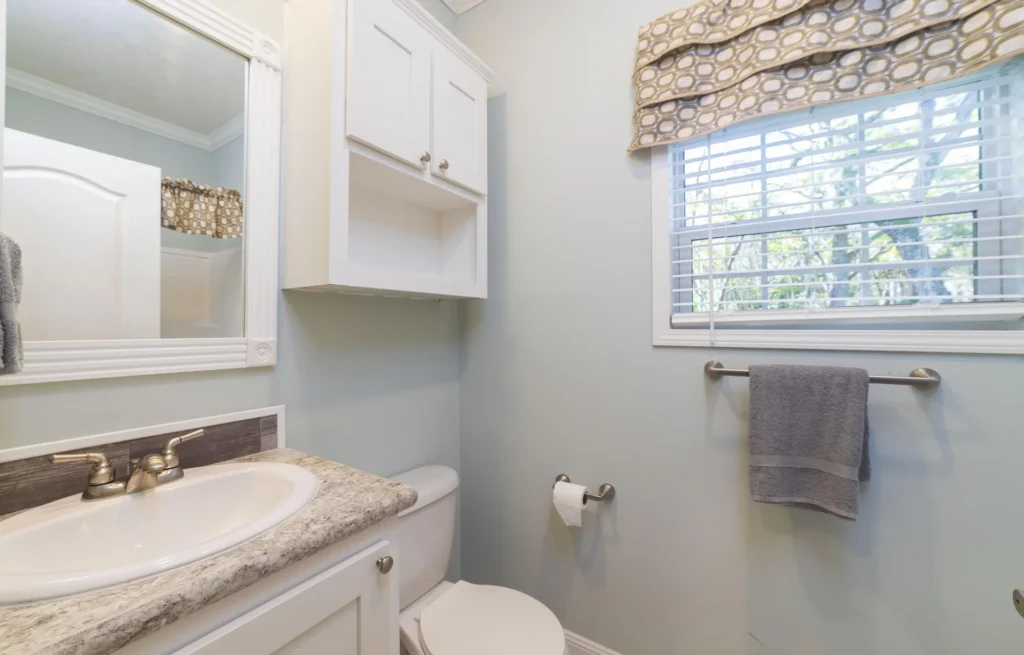 Half-bathroom with granite-effect countertop, white cabinetry, brushed nickel fixtures, and a window with patterned valance.