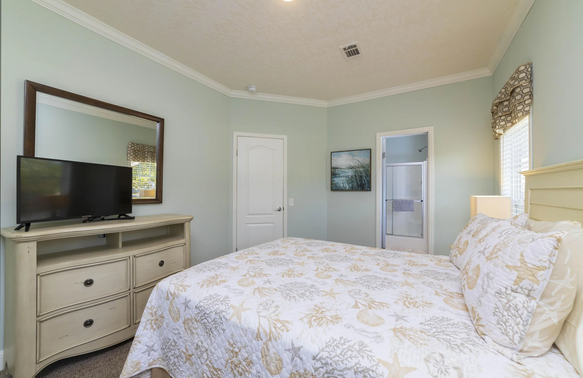 Guest bedroom featuring pastel blue walls, a seashell-patterned quilt, and an en-suite bathroom with glass shower doors.
