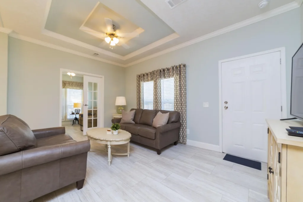 Entryway living area with light wood-look tile flooring, a tray ceiling, and patterned curtains over two windows.