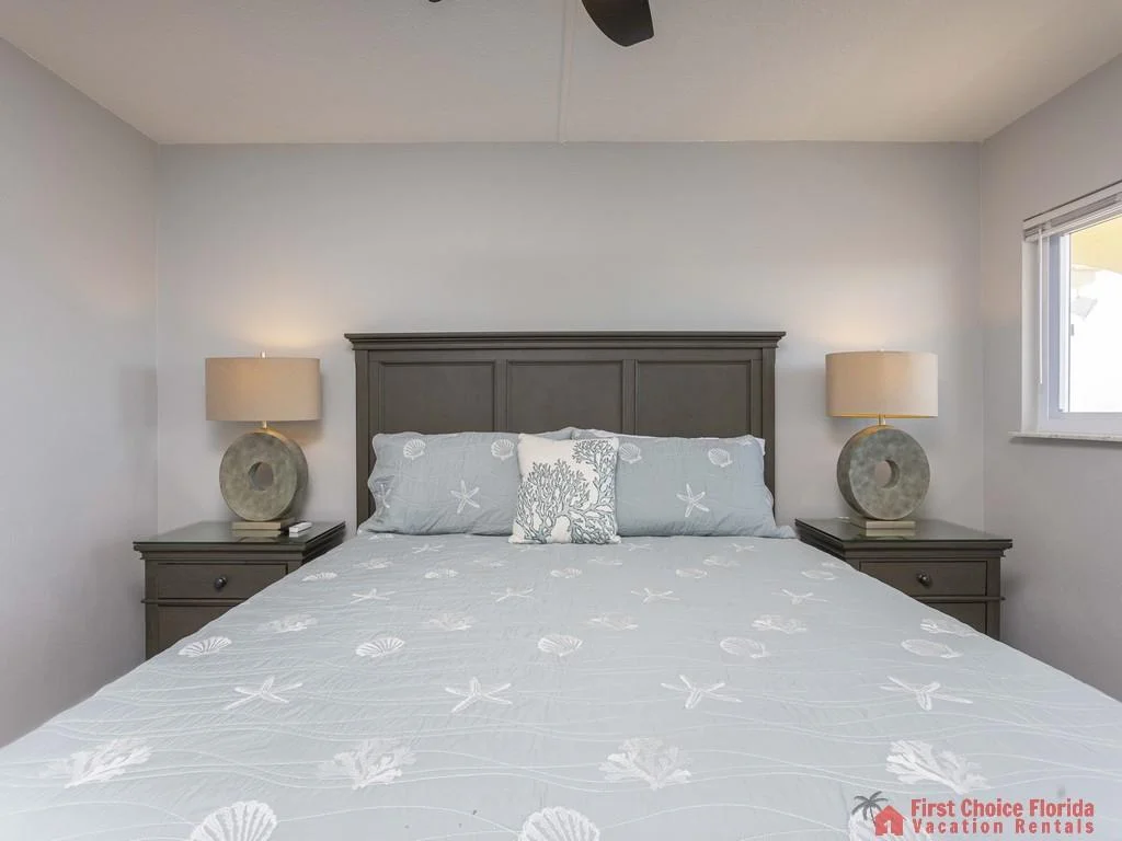 Two dark wood nightstands with circular stone lamps flank the gray paneled headboard in the bedroom.