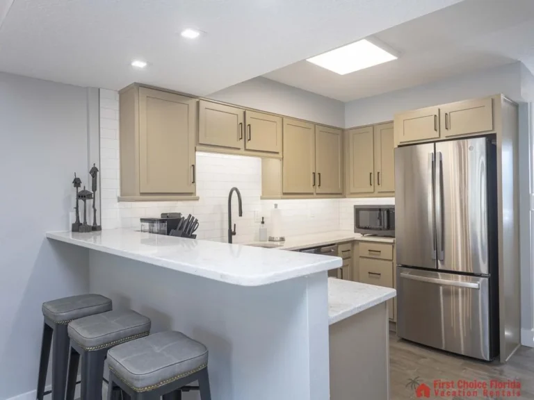 U-shaped kitchen with taupe cabinets, white subway tile backsplash, and stainless steel refrigerator.