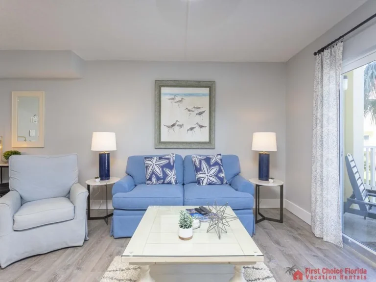 Light wood flooring stretches beneath a blue loveseat flanked by matching lamps and a seaside bird print.