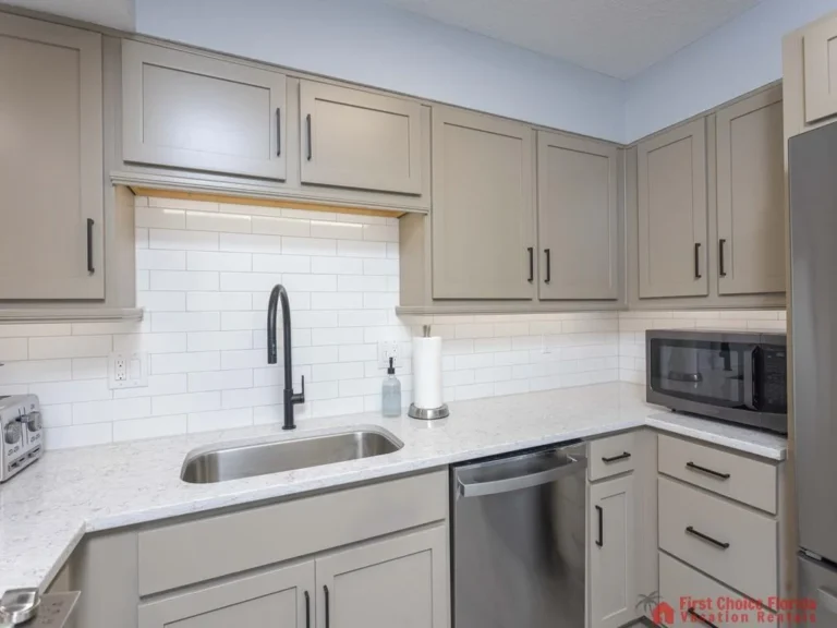 Quartz countertops and taupe cabinets surround a stainless steel sink and dishwasher beneath white subway tile backsplash.