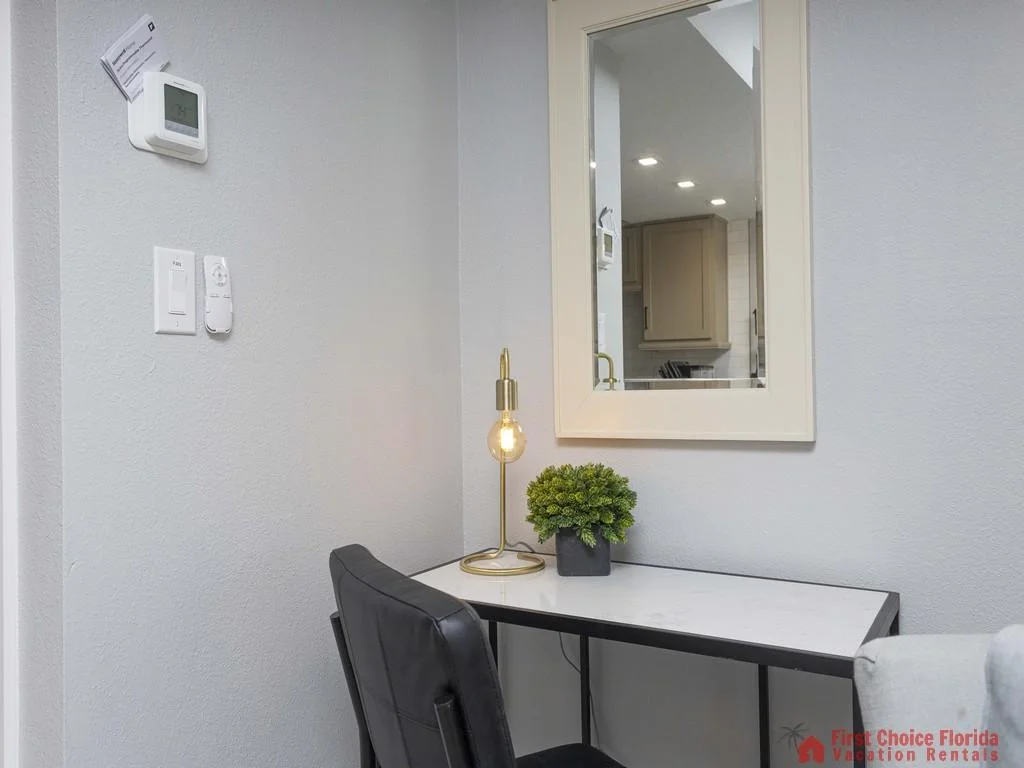 Compact workspace with a black leather chair, white marble-top desk, brass lamp, and wall-mounted mirror.
