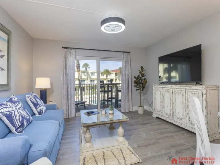 Blue sofa with starfish pillows faces a whitewashed wooden TV cabinet and glass sliding door to the balcony.