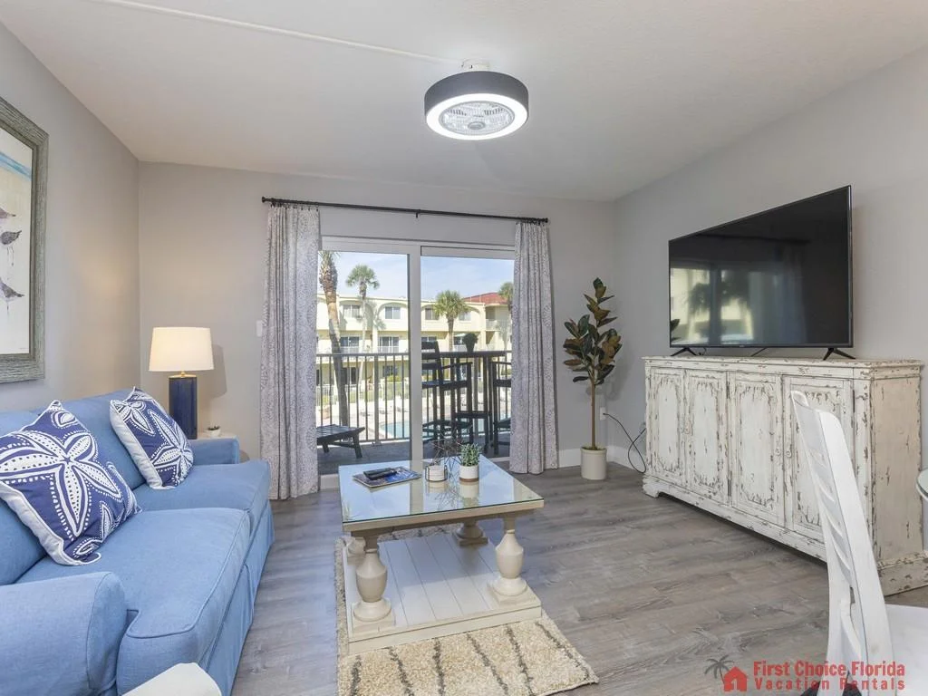 Blue sofa with starfish pillows faces a whitewashed wooden TV cabinet and glass sliding door to the balcony.