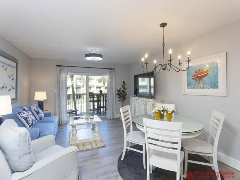 Glass-top dining table with white chairs sits beneath a black metal chandelier in the open living area.