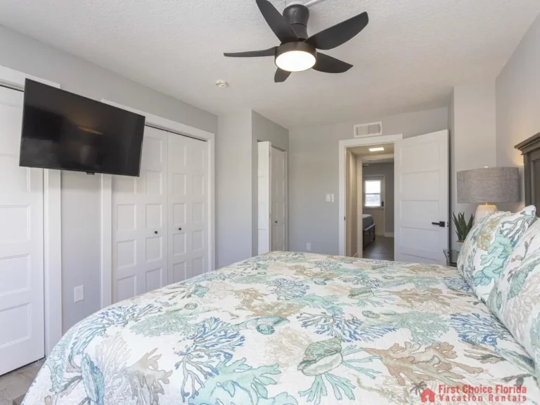 Ceiling fan with five blades and integrated light hangs above the king bed with coral and sea life patterned bedding.
