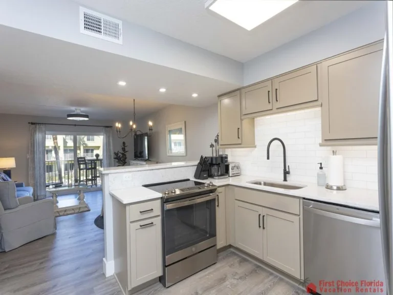 Taupe kitchen cabinets with black hardware surround a white quartz countertop and stainless steel appliances.