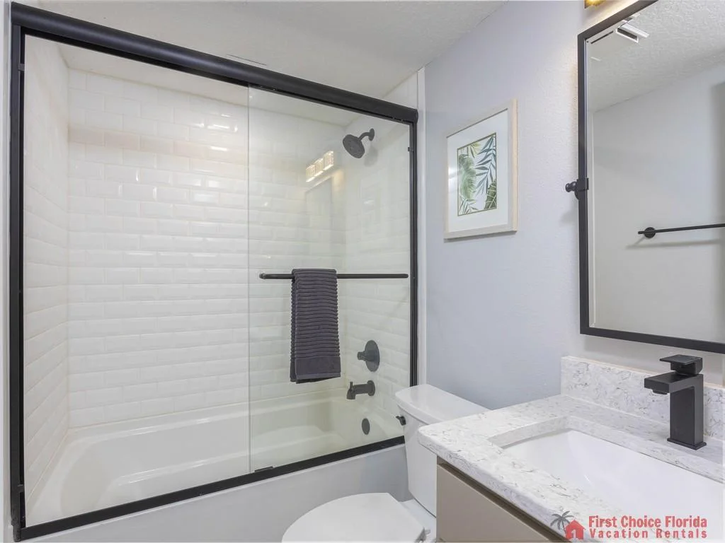 Bathroom features white subway tile shower surround with black framed sliding glass door and matte black fixtures.