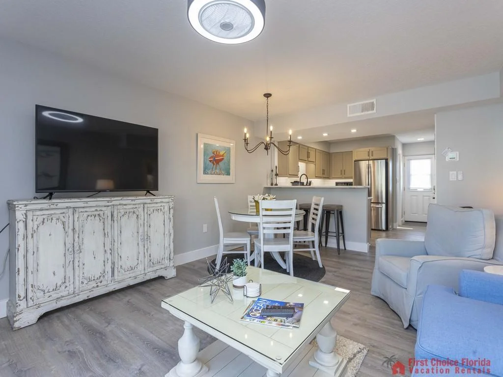 Open living and dining area with distressed white TV console, round table, and light wood flooring.