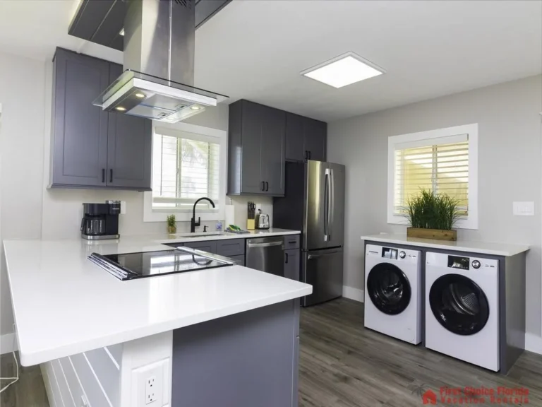 White quartz countertops surround gray shaker cabinets, with stainless steel appliances and a stacked washer and dryer.