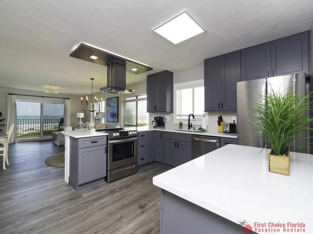 Gray shaker cabinets and stainless steel appliances surround white quartz countertops in the kitchen with ocean views.