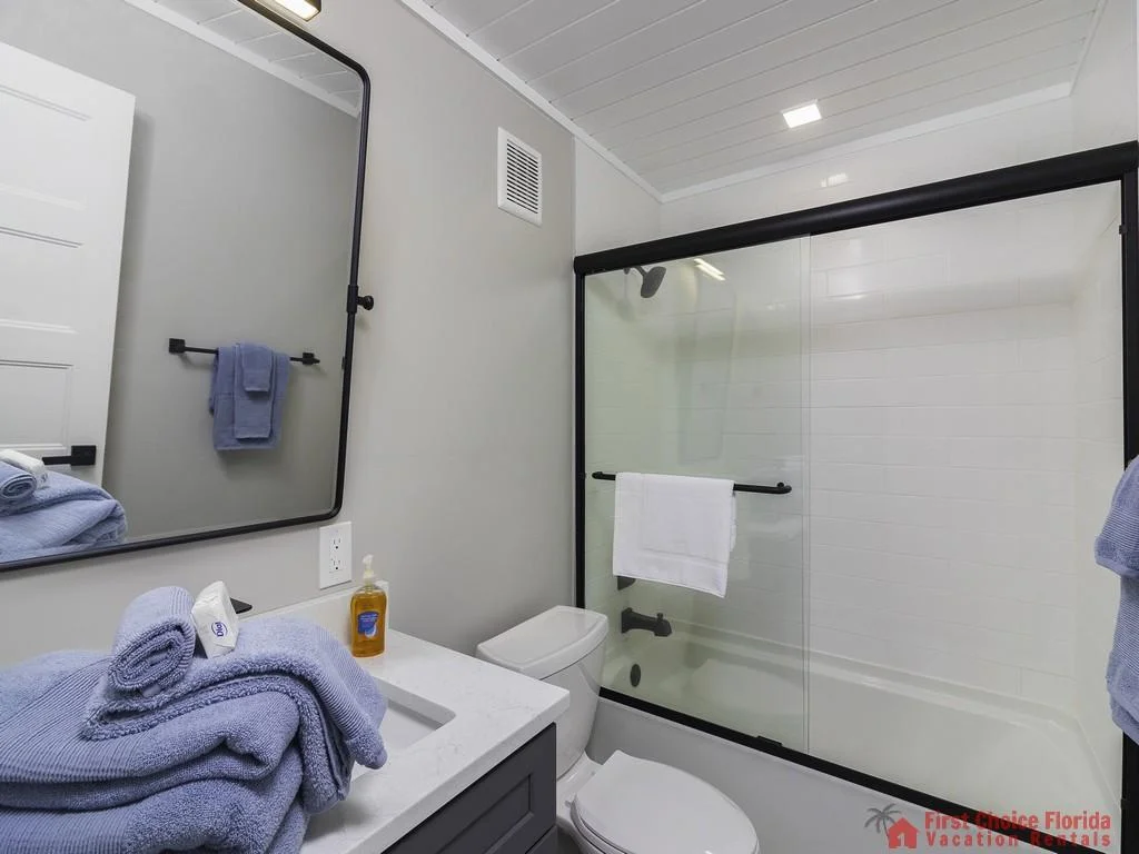 Bathroom with white quartz countertop, charcoal gray vanity, and sliding glass shower doors with black trim.