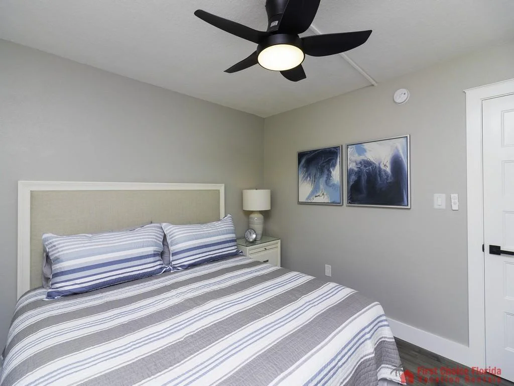 Bedroom with striped gray and blue bedding, white nightstand holding a lamp and clock, and abstract wall art.