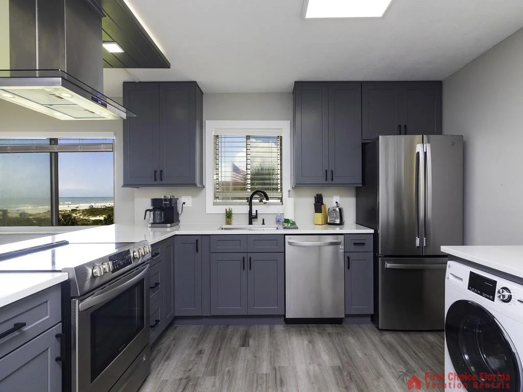 Gray shaker cabinets and white quartz countertops surround stainless steel appliances and a black faucet in the kitchen.