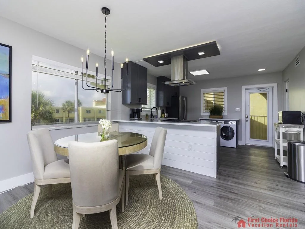 Dining area features a round glass-top table surrounded by four beige upholstered chairs on a woven rug.