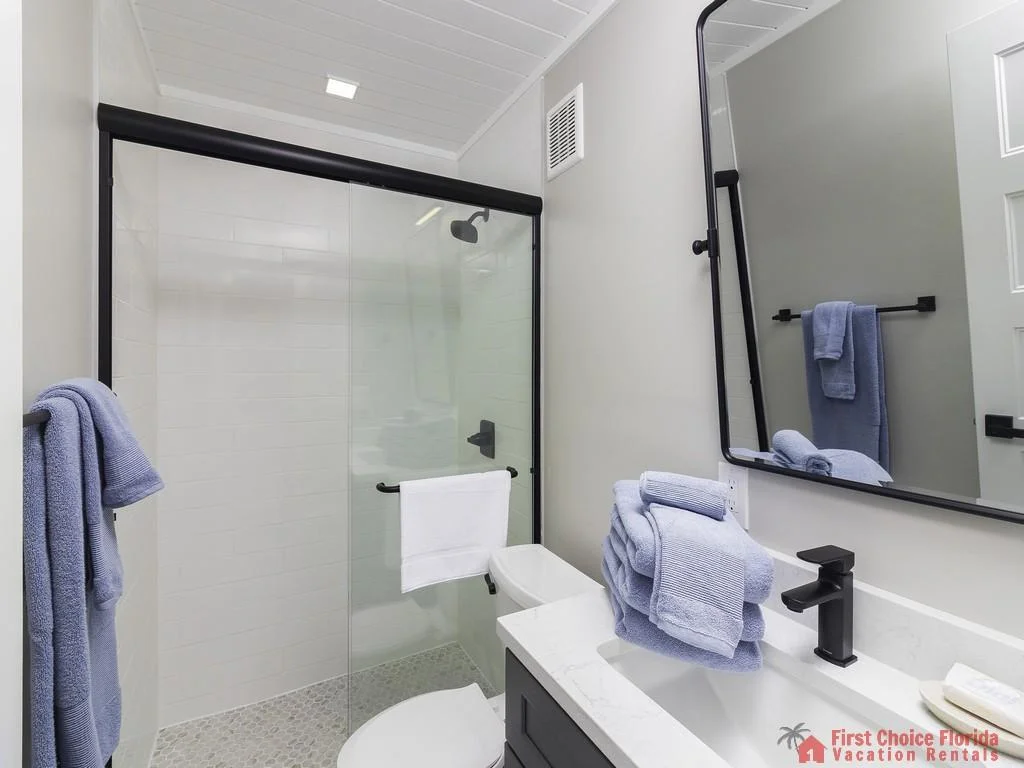 Bathroom features a glass sliding shower door, black fixtures, white subway tile, and a gray vanity with marble countertop.