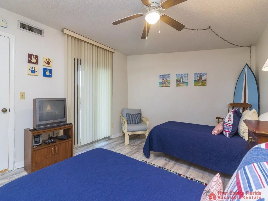 Wall art featuring handprints and lighthouses adds color above twin beds dressed in navy quilts and striped pillows.