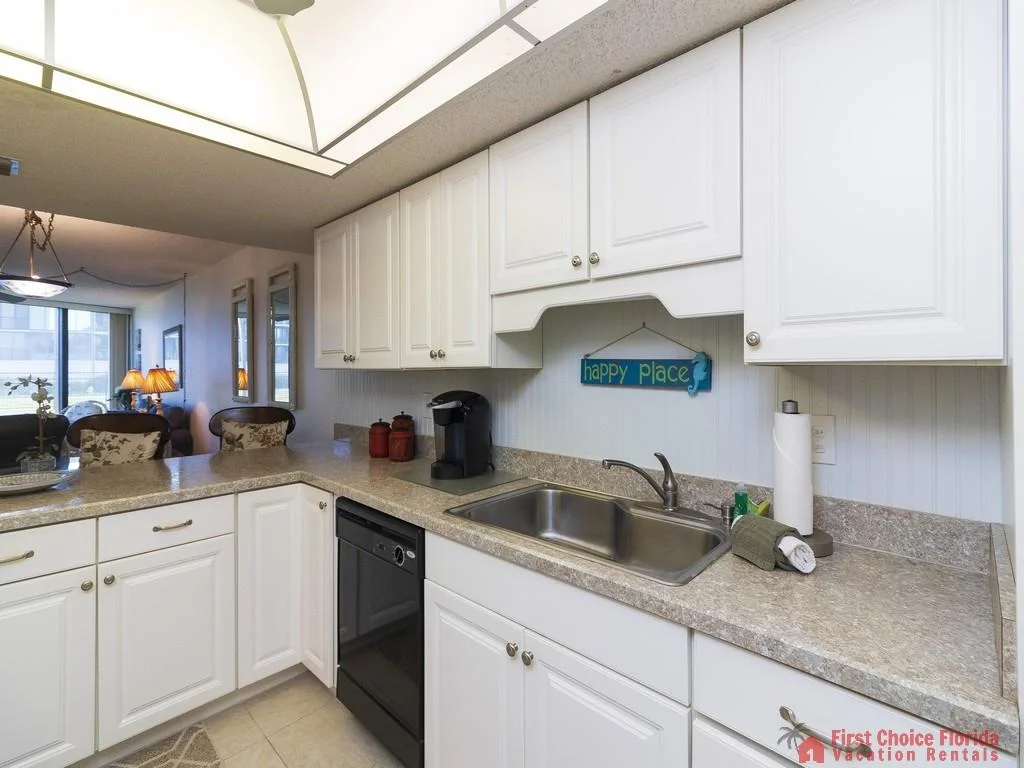 White cabinets and granite-patterned laminate counters surround a stainless steel sink and black dishwasher.