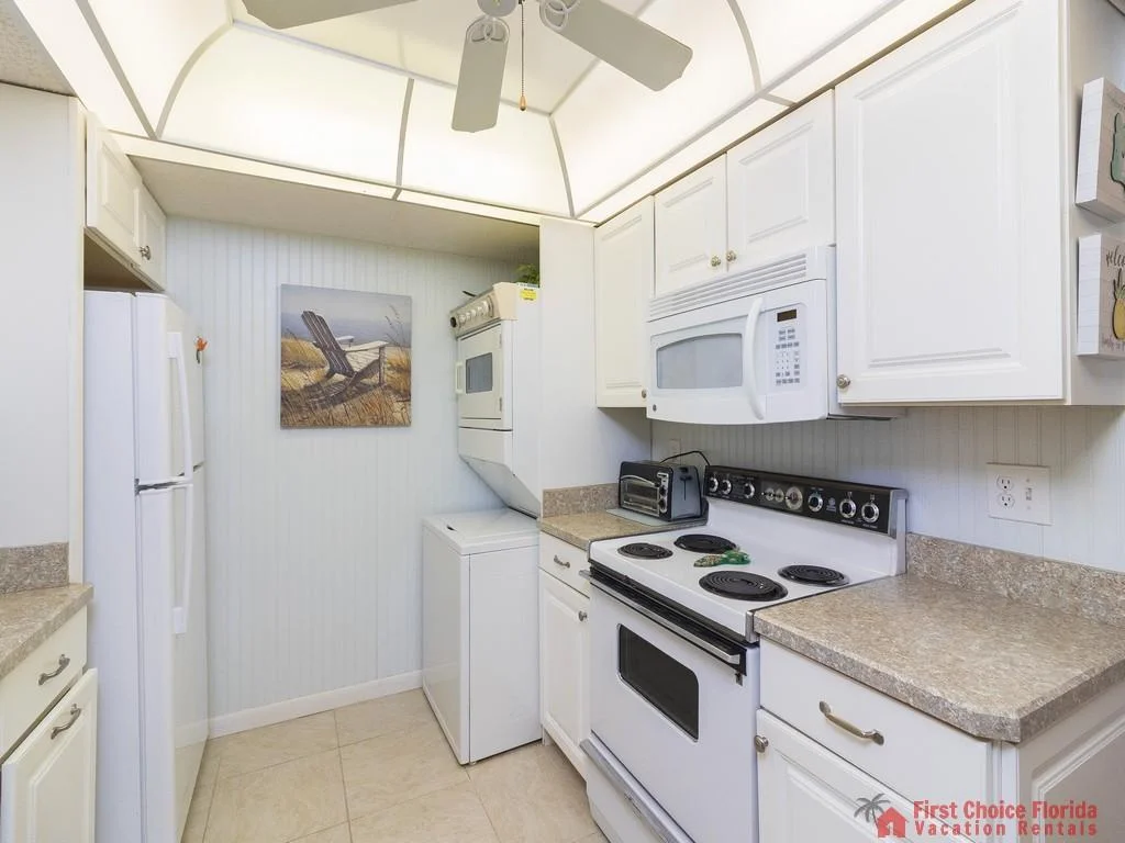 White cabinetry surrounds a compact kitchen with stacked washer-dryer, electric stove, and speckled laminate counters.