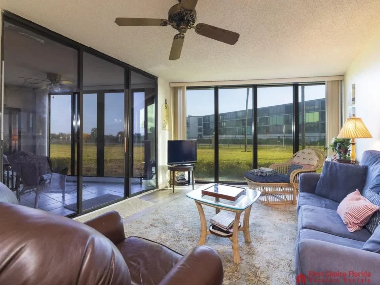 Leather armchair and blue sofa flank a glass-top coffee table in the living room with floor-to-ceiling windows.