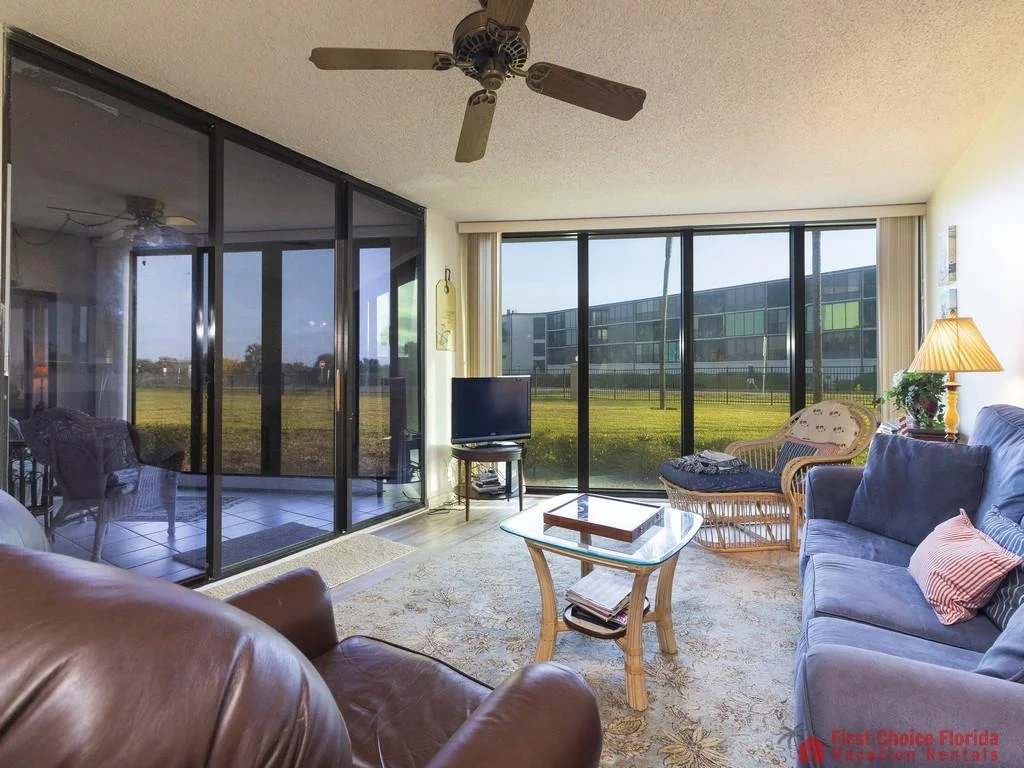 Leather armchair and blue sofa flank a glass-top coffee table in the living room with floor-to-ceiling windows.