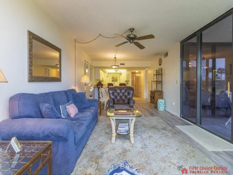 Blue fabric sofa and tufted leather armchair face a glass coffee table on a patterned rug in the living room.