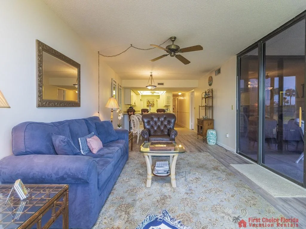 Blue fabric sofa and tufted leather armchair face a glass coffee table on a patterned rug in the living room.