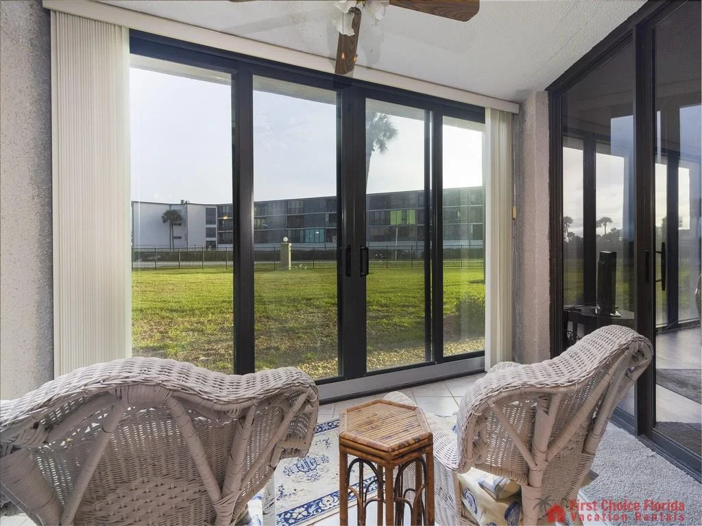 Two white wicker chairs face sliding glass doors opening to a grassy courtyard in the sunroom.