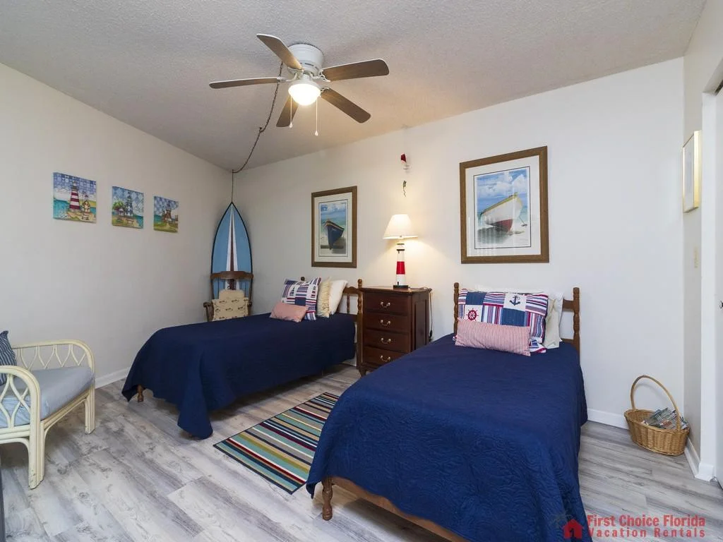 Two twin beds with navy quilts flank a dark wood dresser under framed boat prints in the bedroom.