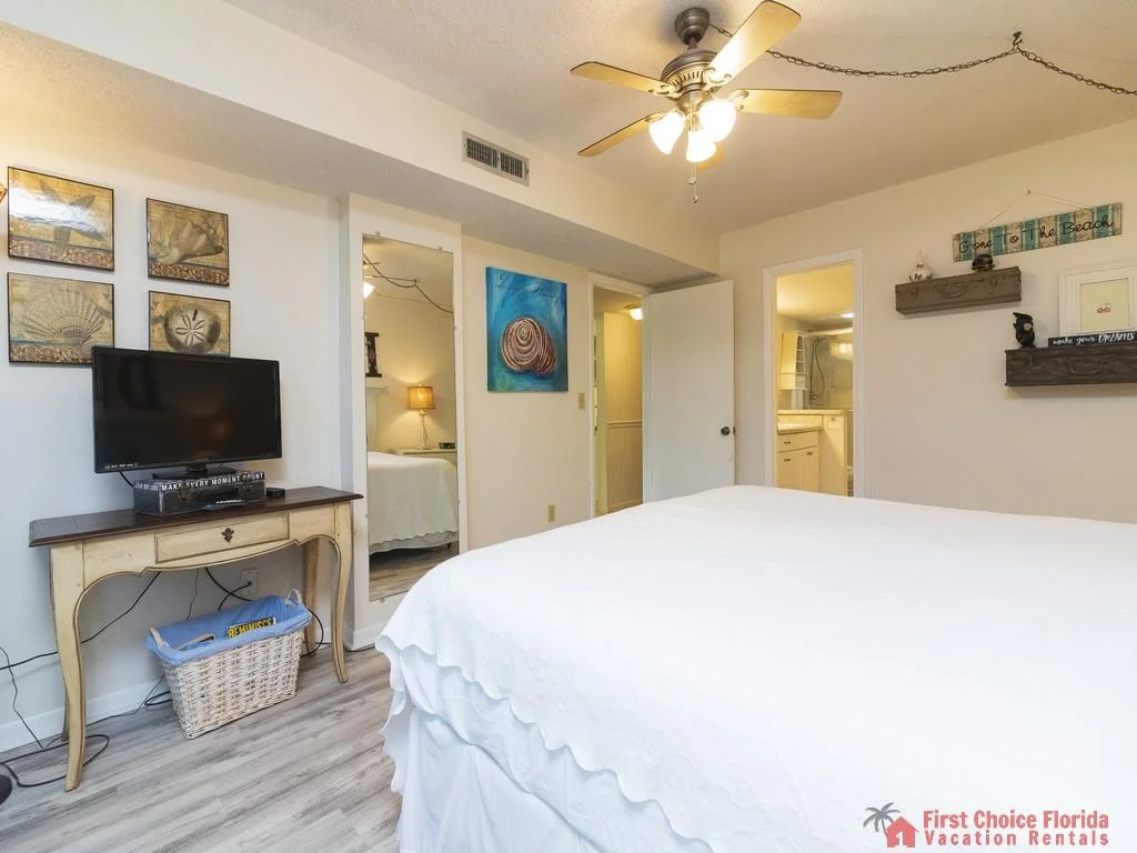 Queen bed with white quilted bedding faces a vintage-style console table holding a flat-screen TV.