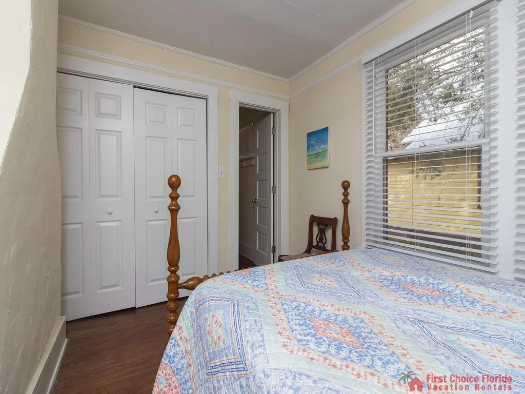 Spindle-post bed with patterned blue and orange quilt sits next to a large window with white blinds.