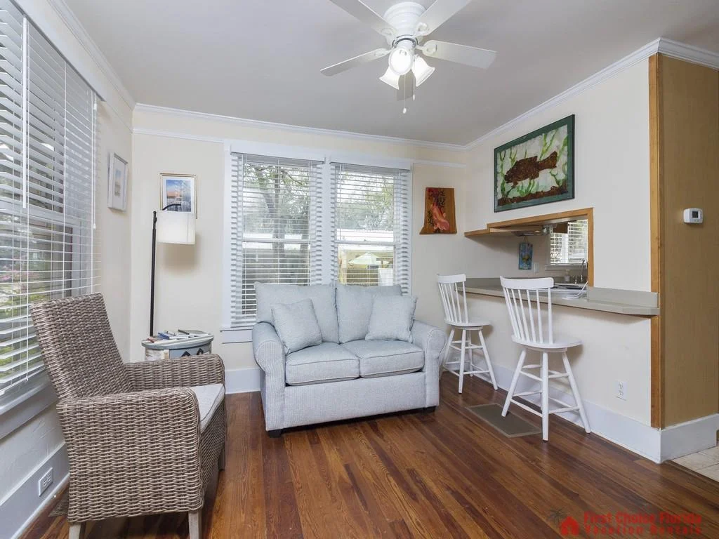 Wicker armchair and light blue loveseat face the kitchen pass-through with white bar stools and fish artwork.