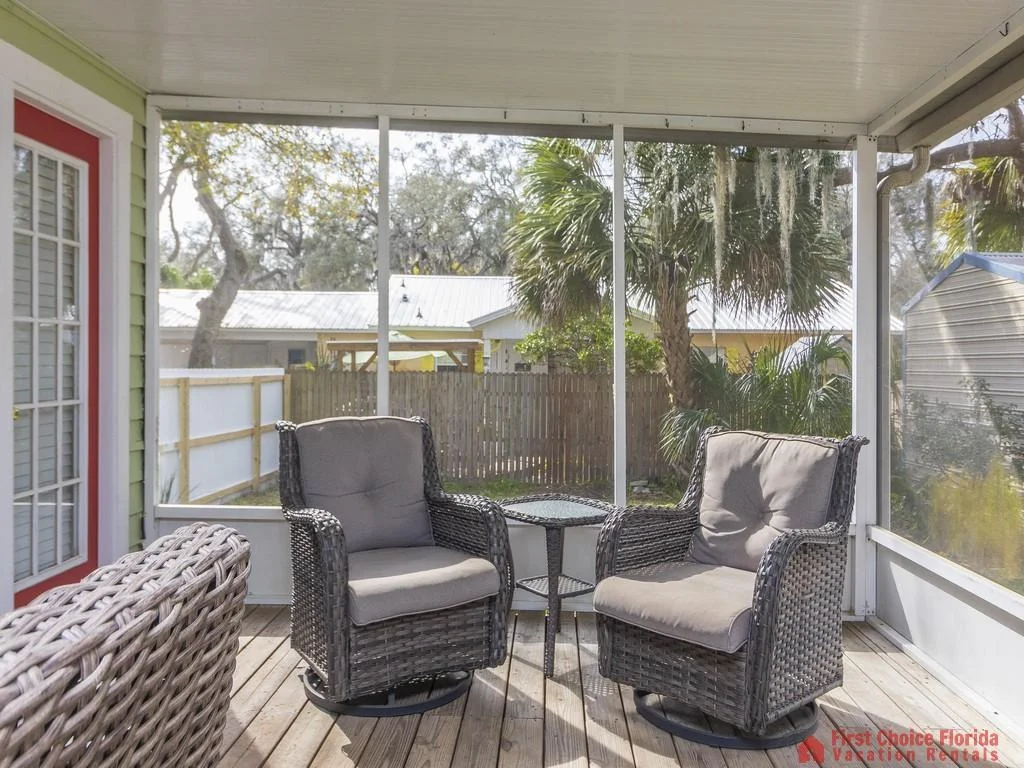 Two gray cushioned wicker swivel chairs face each other across a wicker side table on the screened porch.