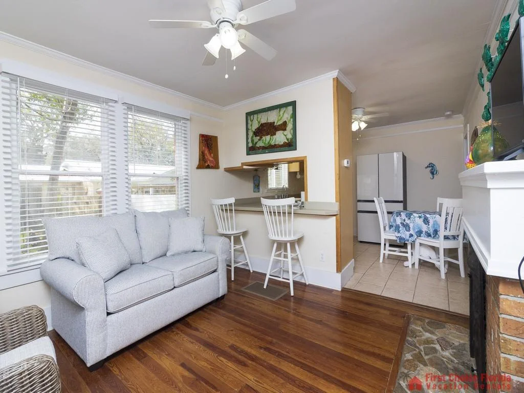 White bar stools line the kitchen pass-through overlooking the living room with striped gray loveseat and hardwood floors.