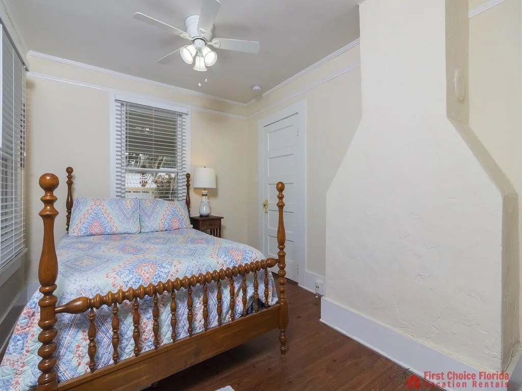 Spindle-post wooden bed with patterned blue and orange bedding sits against pale yellow walls and hardwood floors.