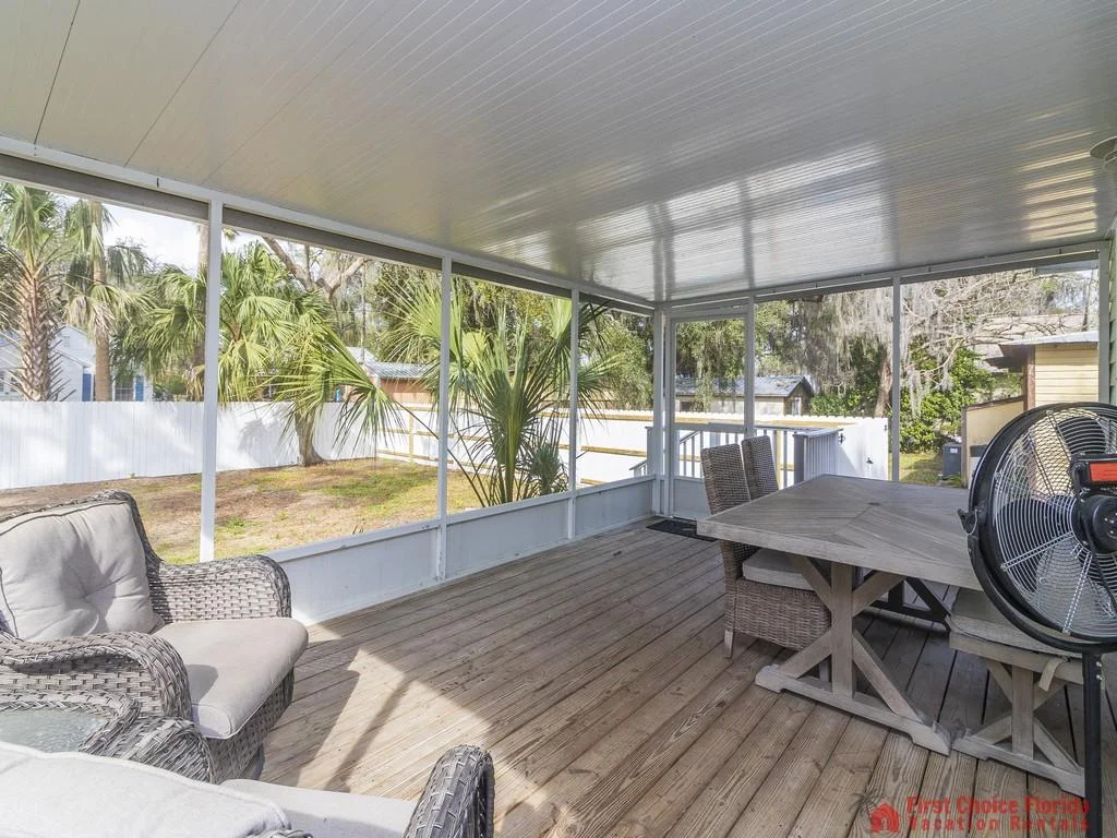 Screened porch with natural wood plank flooring, gray wicker chairs, and a rectangular dining table.