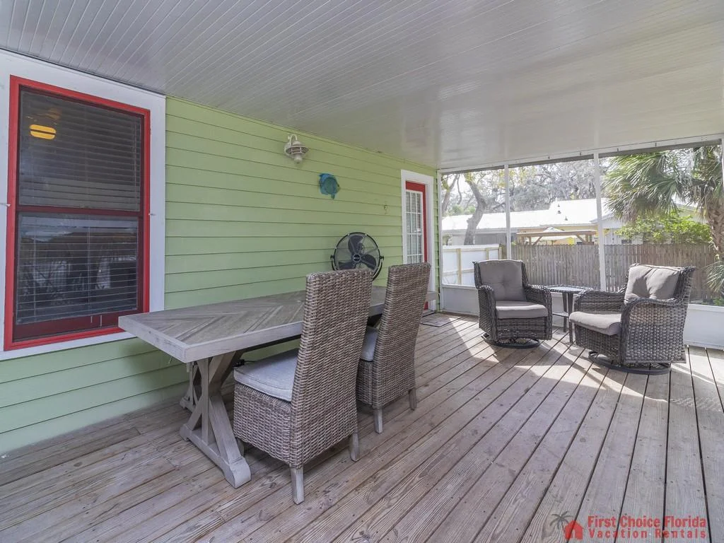 Screened porch features natural wood flooring, green siding, red-trimmed windows, and wicker dining and lounge chairs.