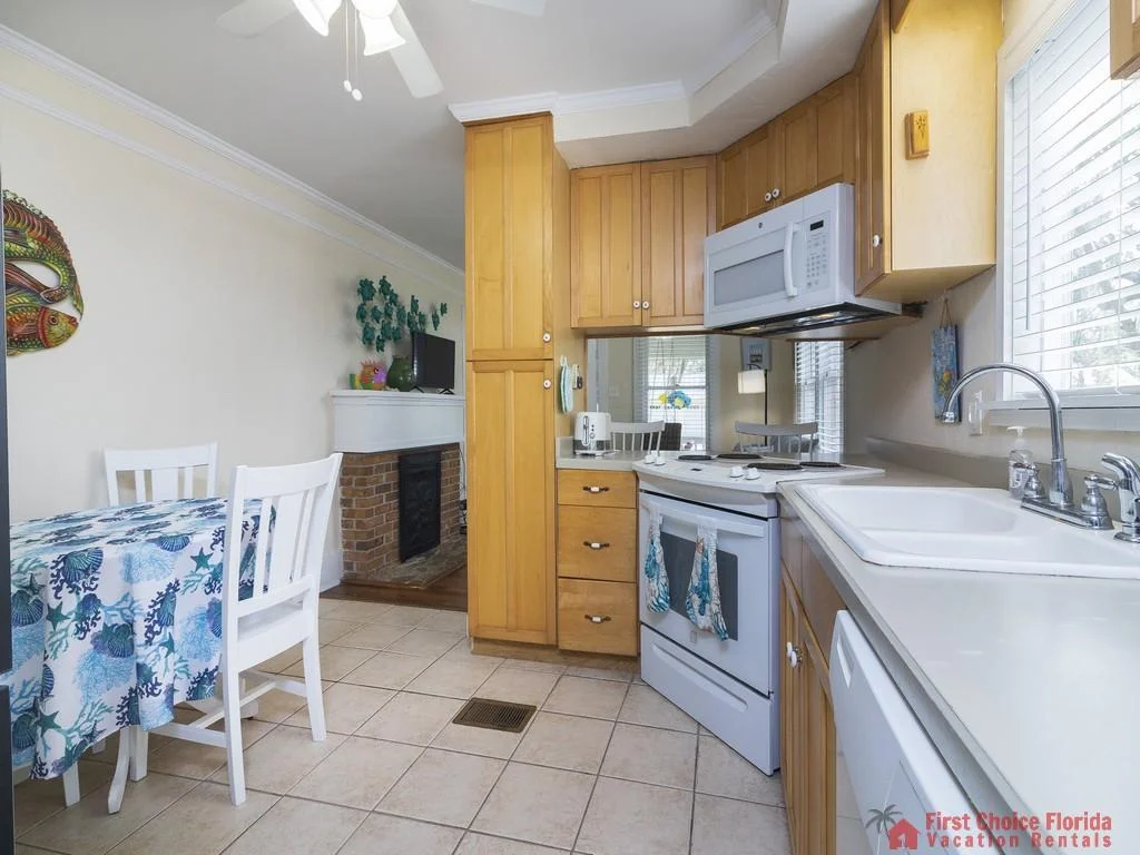 White appliances, including stove and microwave, complement light wood cabinetry and tiled floors in the kitchen.
